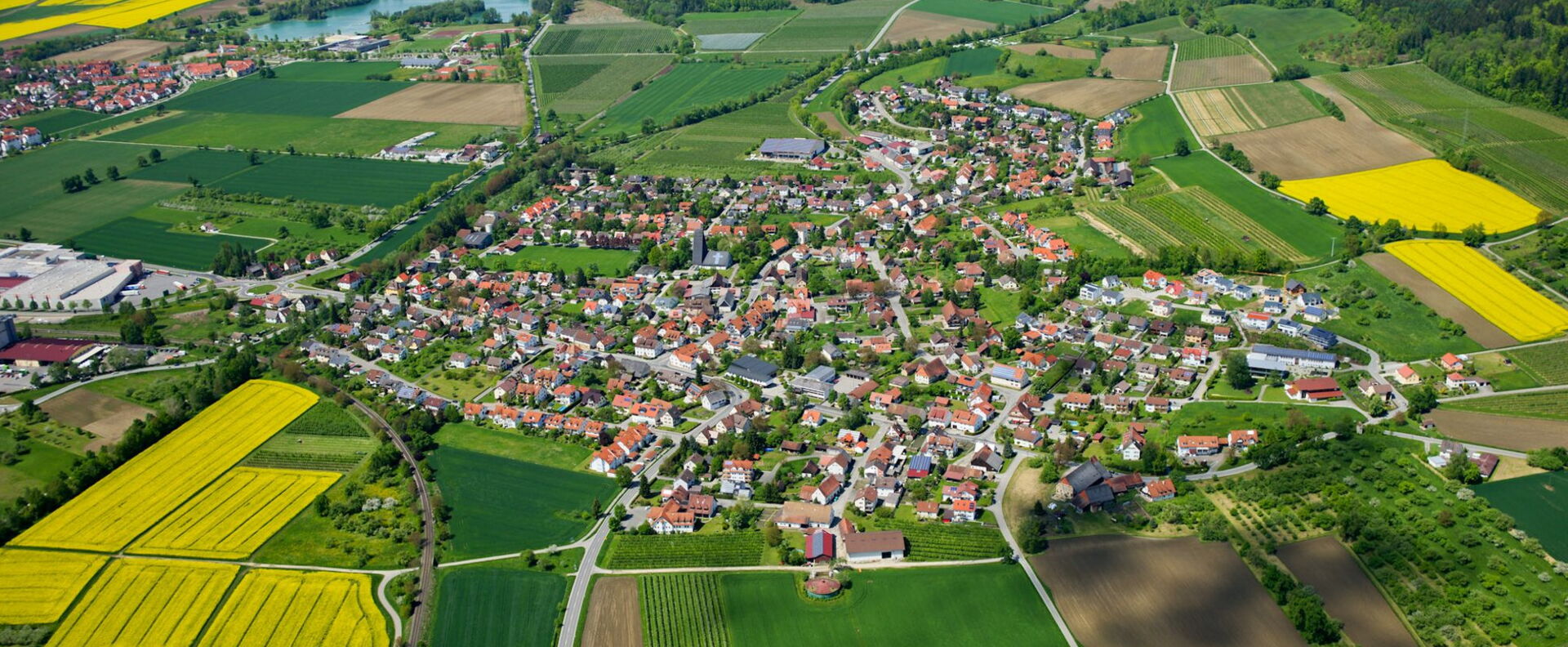 Luftbild einer Stadt umgeben von grünen Agrarflächen & gelben Rapsfeldern - Region Bodensee