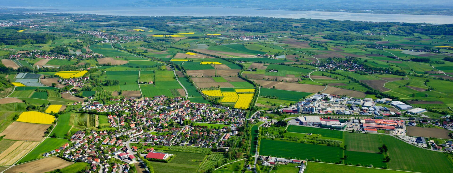Luftbild der Region am Bodensee mit Blick auf Kleinstadt mit Gewerbegebiet - umgeben von grünen Agrarflächen