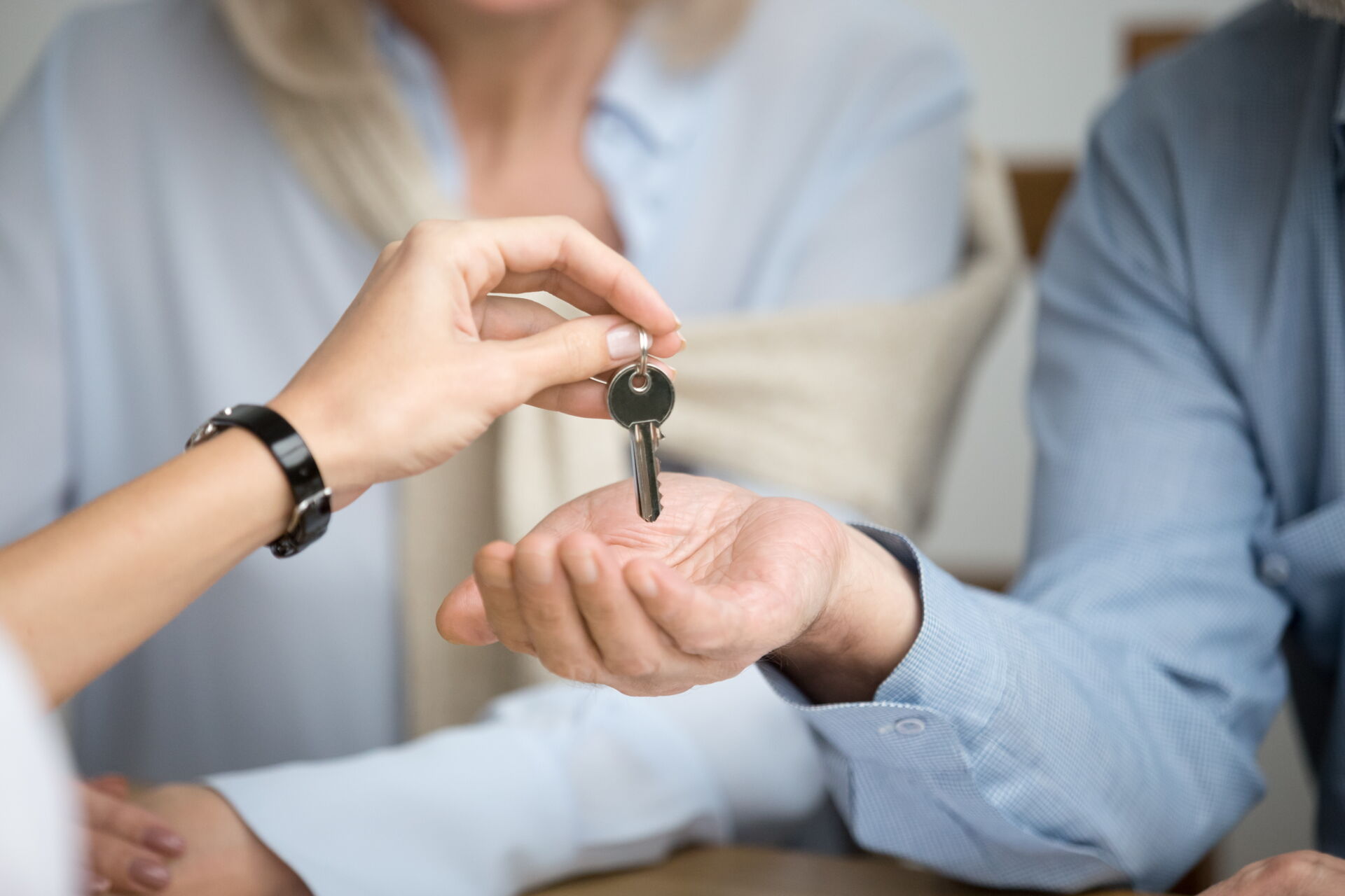 Schlüsselübergabe bei Immobilienkauf - Eine Frauenhand legt Schlüssel in eine geöffnete männliche Hand