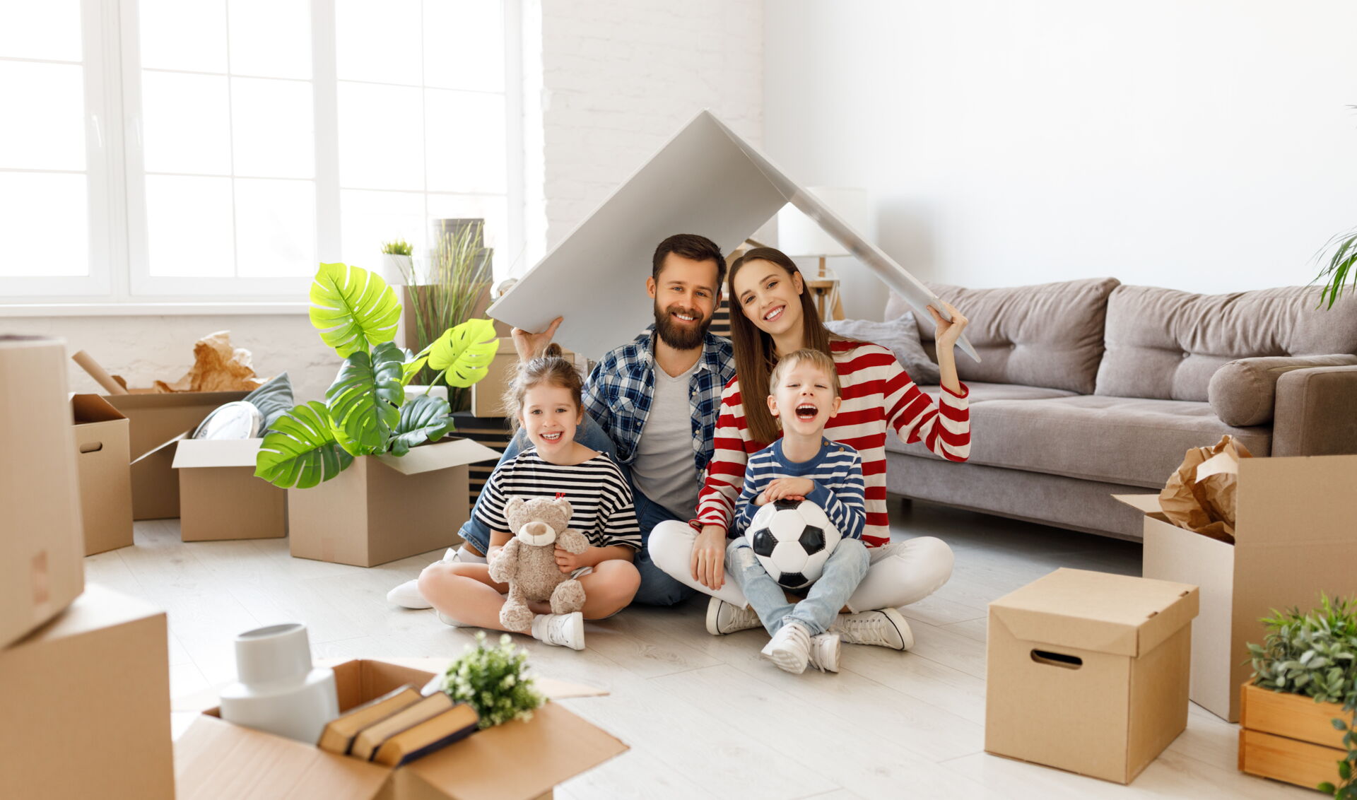 Fröhliche junge Familie mit zwei Kindern zwischen Umzugskisten im neuen Wohnzimmer