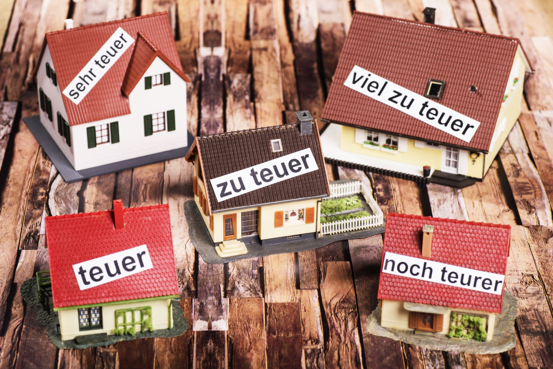 Fünf kleine Modellhäuser von Einfamilienhäusern - alle mit Beschriftung von teuer bis viel zu teuer